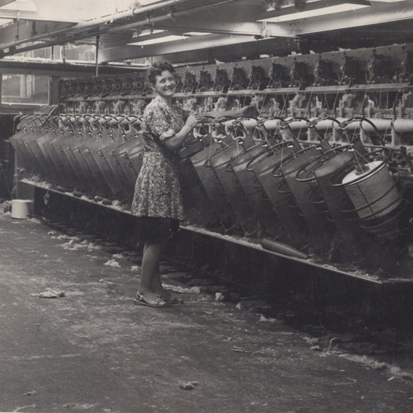 Archive photograph of a mill worker standing beside a row of spinning frames at Kearsley Mill