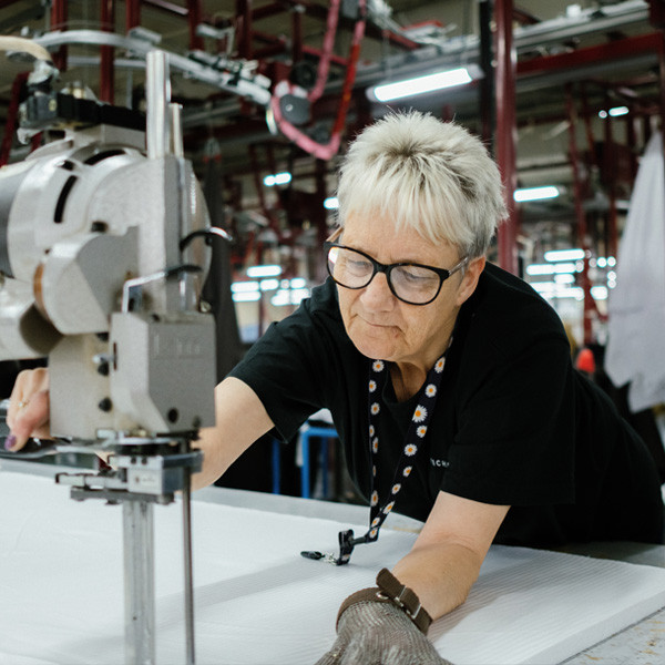 An operator guiding a cloth-cutting machine across white fabric at Kearsley Mill