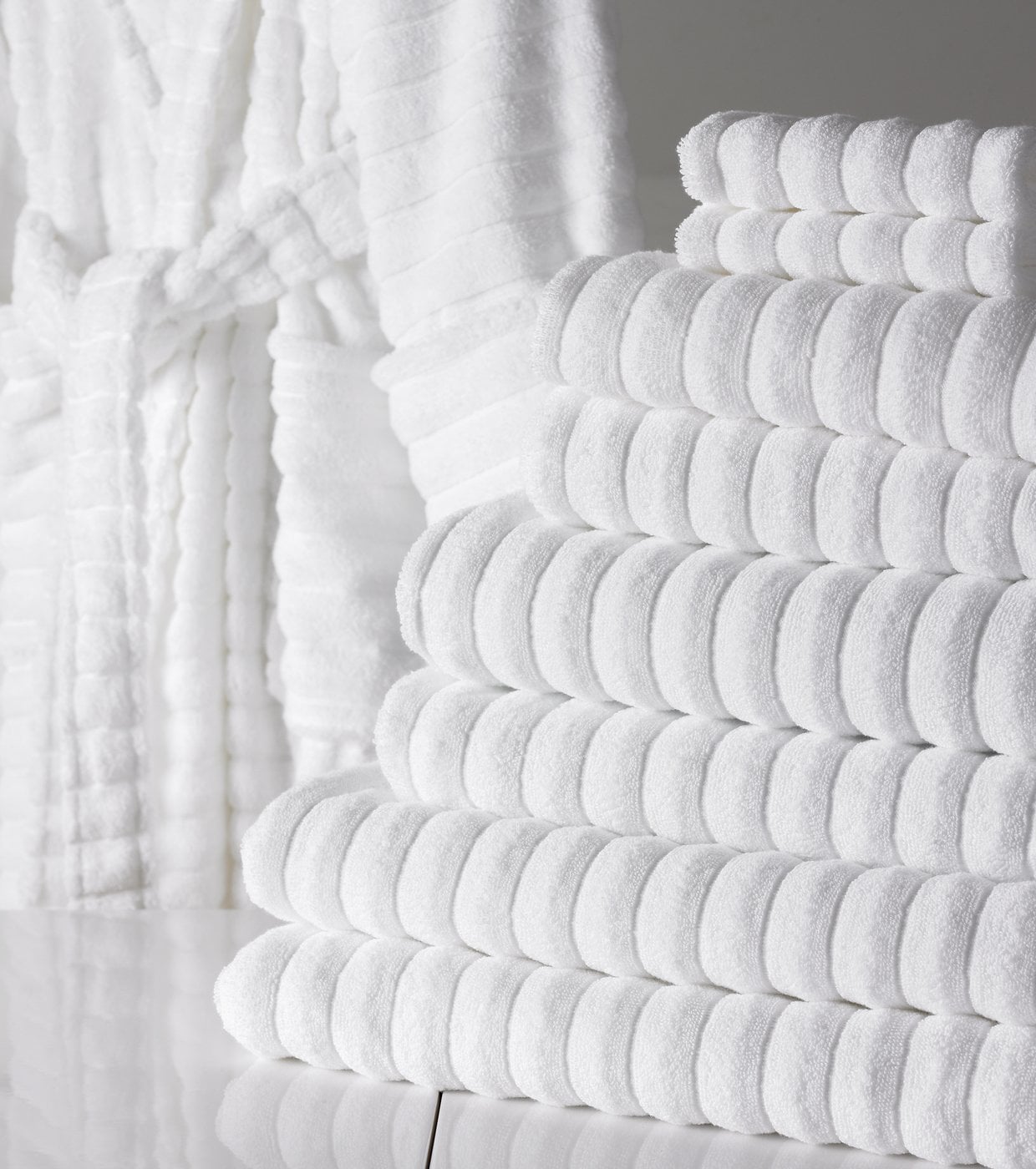 White ribbed hotel towels stacked beside a matching bathrobe