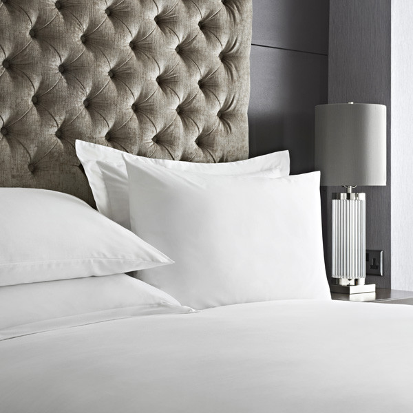 Crisp white cotton-rich bed linen on a hotel bed with a buttoned headboard