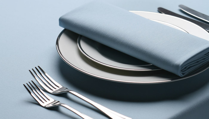 A place setting on tan Signature table linen with a folded napkin, plates and silver cutlery