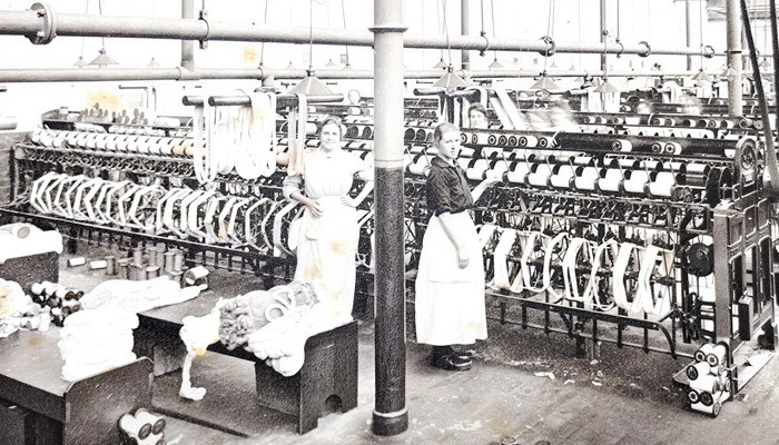 Two workers winding cotton from hanks to bobbins at rows of winding frames